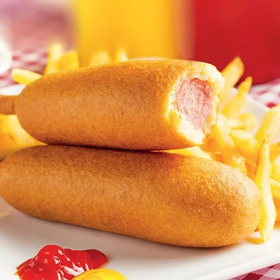 Deux corn dogs dorés, dont un coupé laissant voir la saucisse, servis avec des frites et des sauces.
