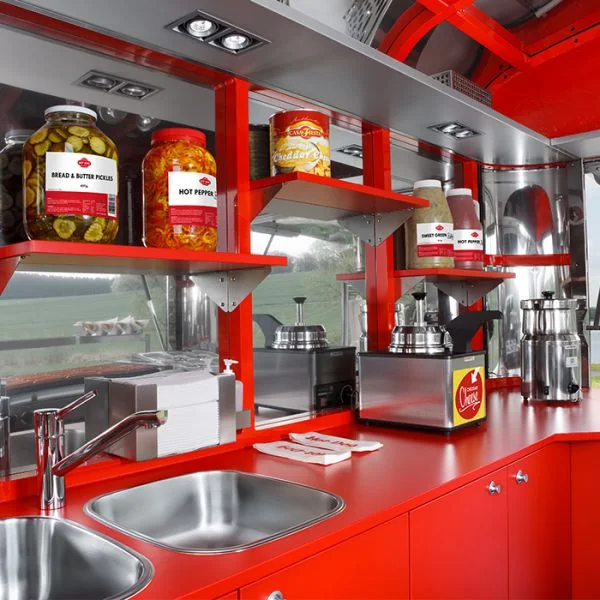 Intérieur rouge et métallique d’une remorque hot dog avec évier, plan de travail et étagère à garnitures.